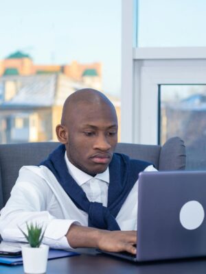 Business professional concentrating on work at a laptop in a modern office with a city view.