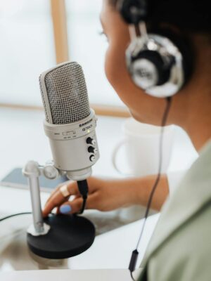 Woman using a microphone and headphones indoors, focusing on recording a podcast or voiceover.